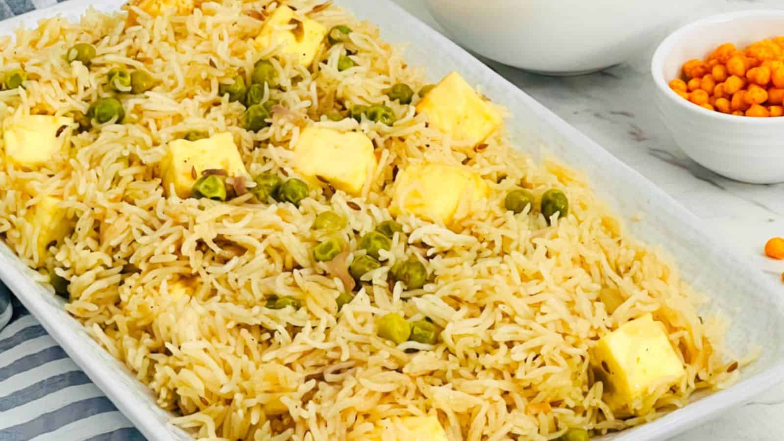 A dish of Paneer Peas Pulao in a rectangular serving tray, accompanied by a bowl of boondi raita.