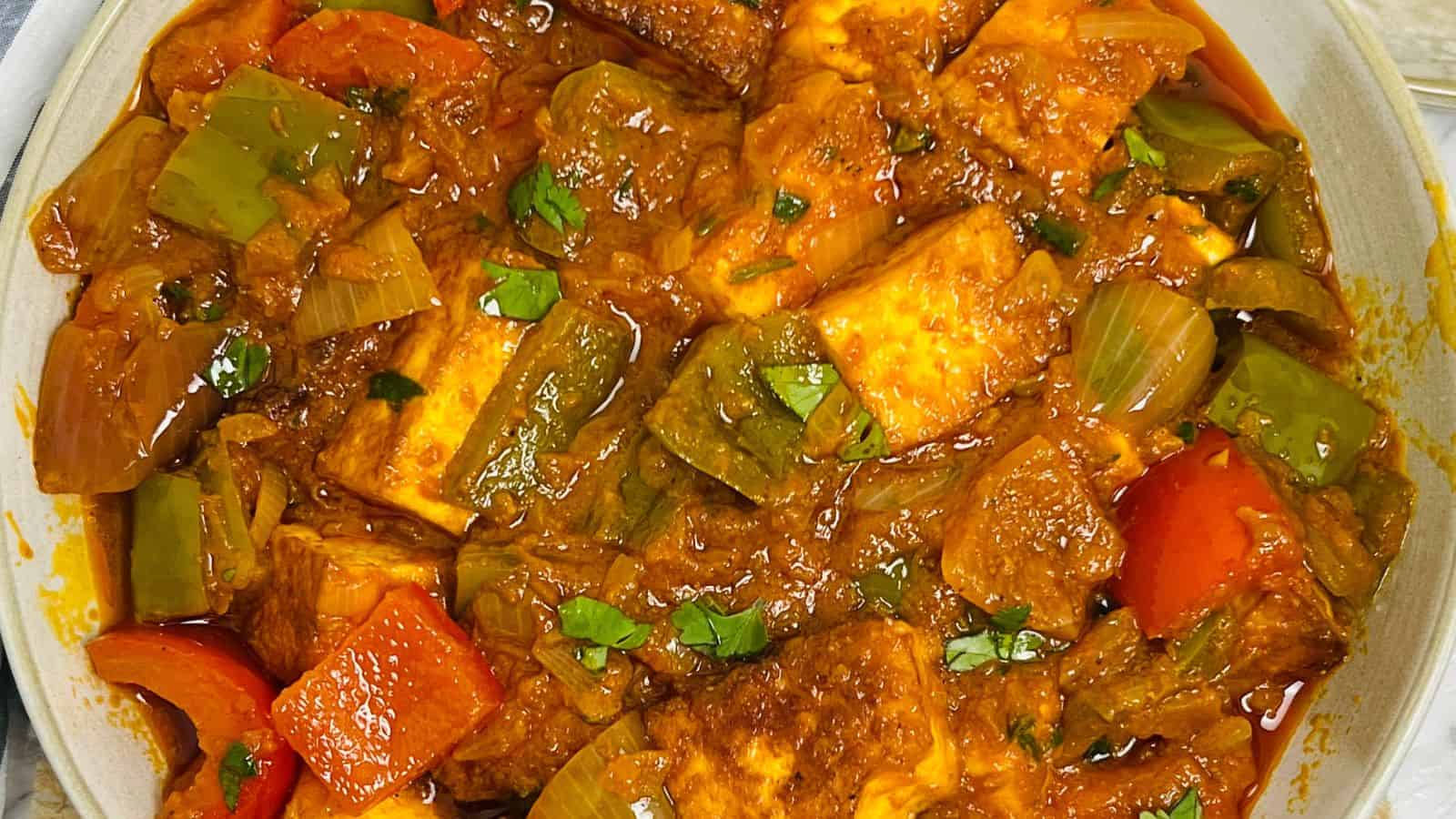 A close-up of Paneer Sabzi featuring chunks of paneer with bell peppers in a rich, spicy tomato-based sauce, garnished with herbs.