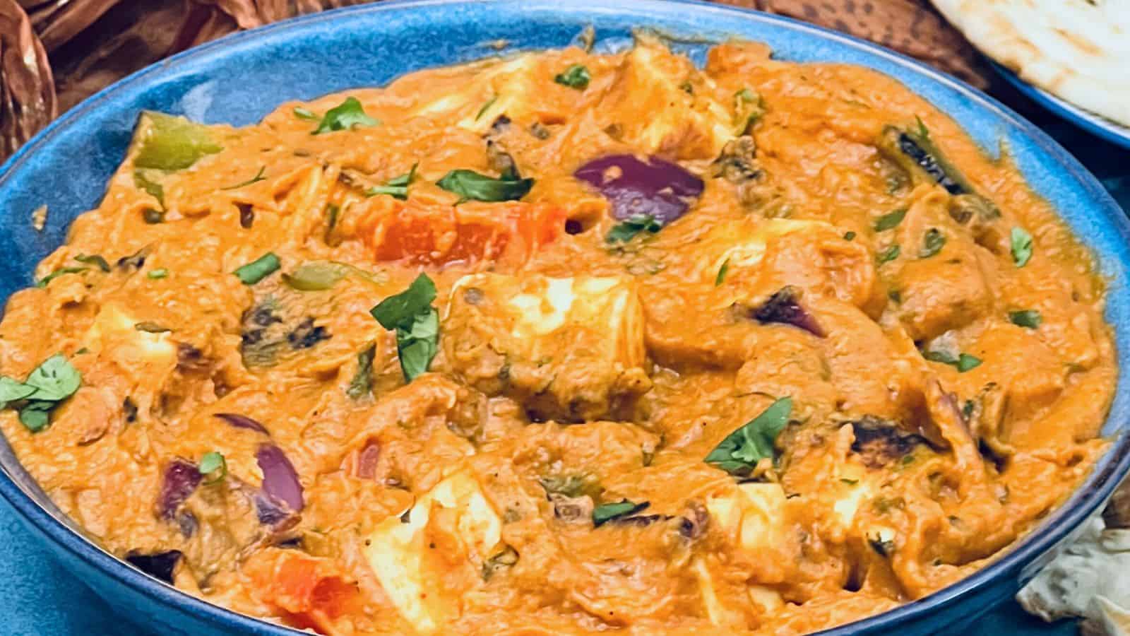 A vibrant dish of Paneer tikka masala garnished with cilantro in a blue bowl, served alongside naan bread.