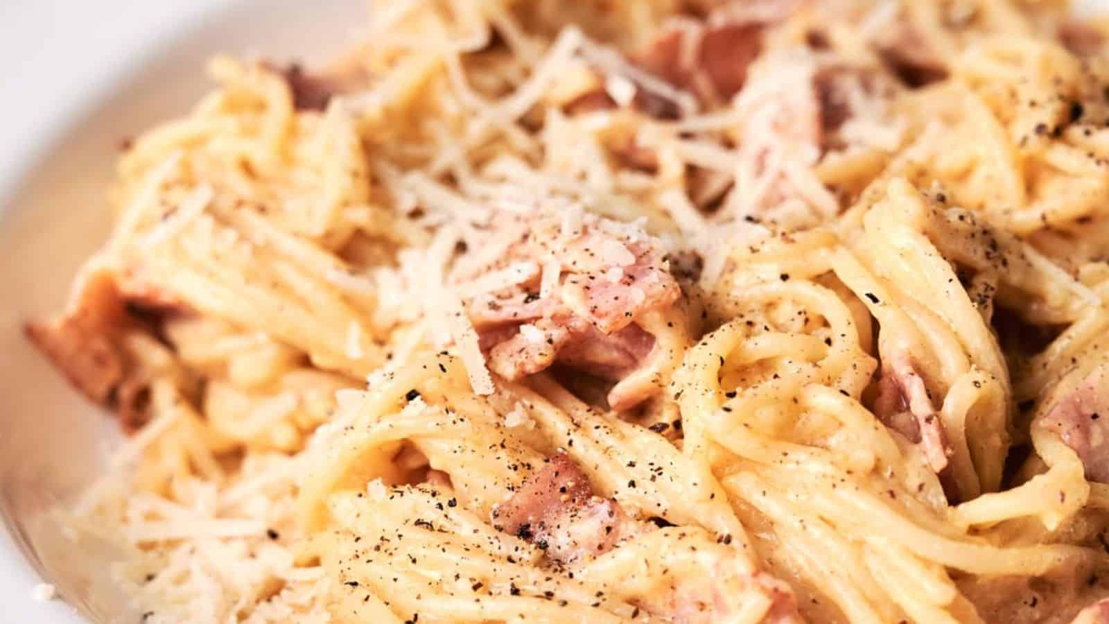 A close-up image of spaghetti carbonara topped with grated cheese and freshly ground black pepper.