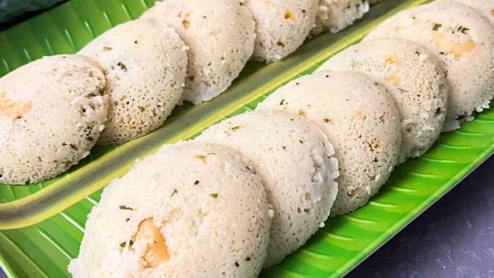 A row of idli, a traditional south indian steamed rice cake, served on a green banana leaf.