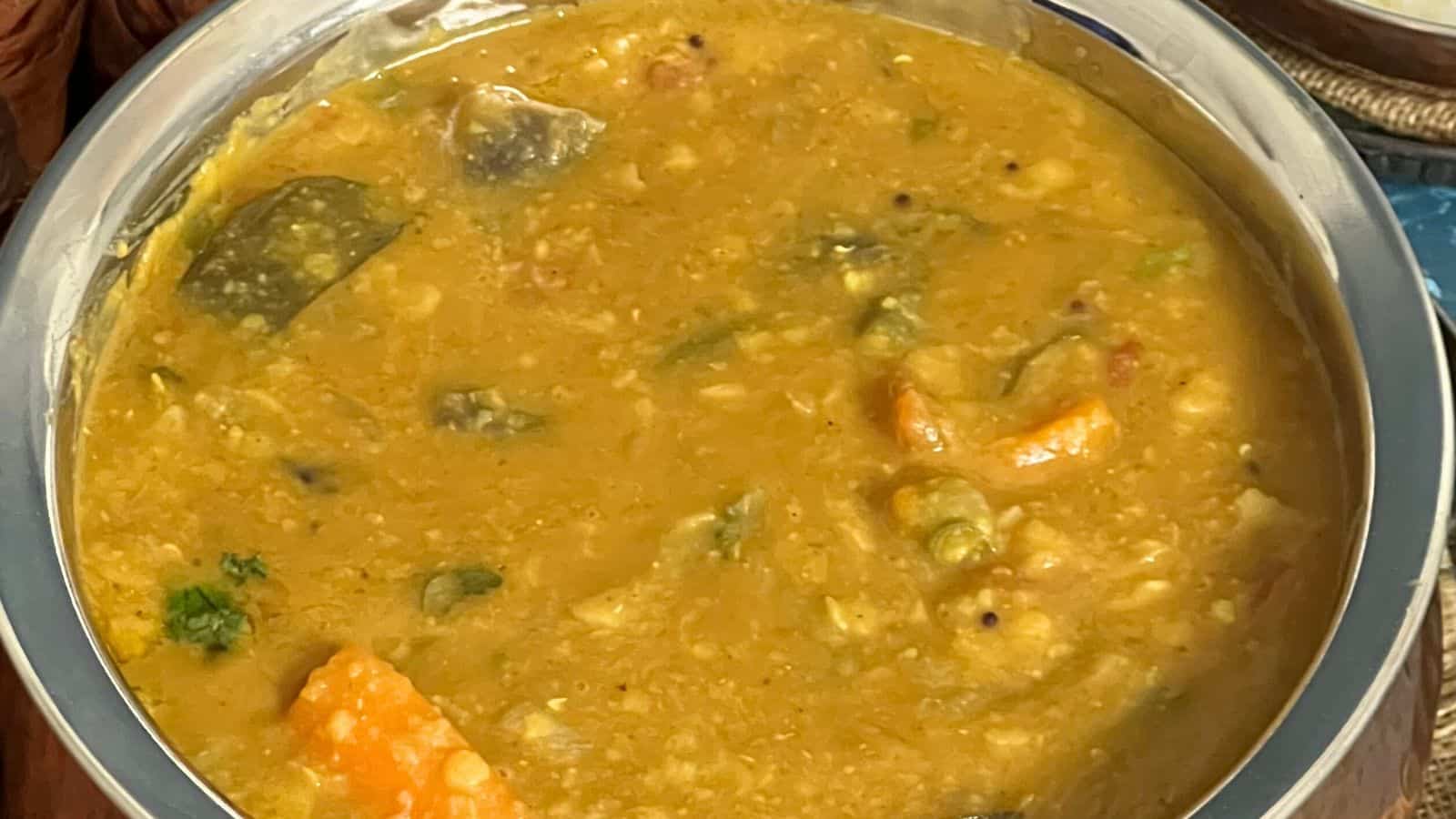 Close-up of a bowl filled with a thick, yellow-colored stew containing visible pieces of vegetables and herbs.