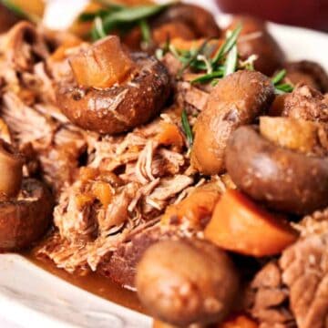 Slow cooker pot roast with mushrooms and carrots garnished with fresh rosemary.