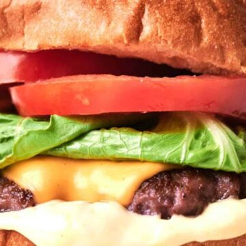 Close-up of a copycat smash burger with lettuce, tomato, and a thick beef patty on a sesame seed bun.