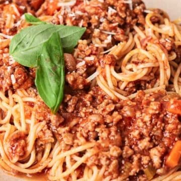 A plate of spaghetti topped with meat sauce and a fresh basil leaf, served with a fork on the side.
