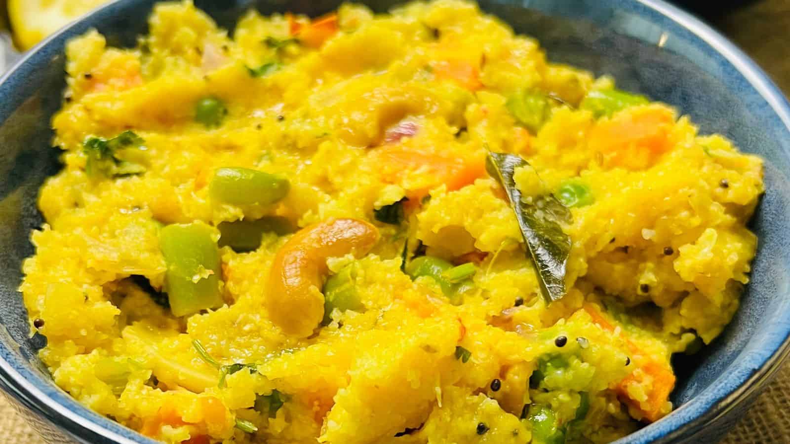 A bowl of colorful upma, an indian dish made with rice and lentils, garnished with cashews and herbs.