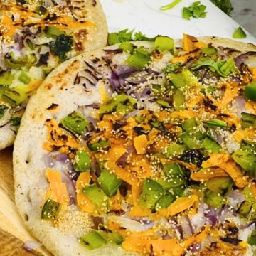 Two vegetable-topped uttapam with a side of sauce.
