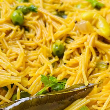 A bowl of cooked vermicelli noodles garnished with green peas and a bay leaf.