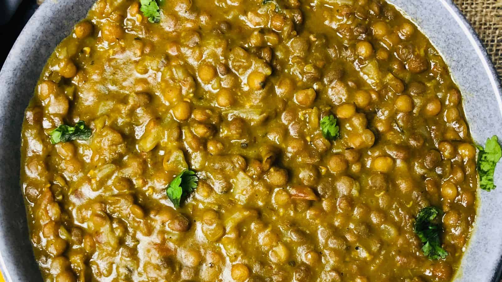 A bowl of Whole Masoor Dal garnished with fresh cilantro, consisting of cooked chickpeas in a spiced, saucy mixture.