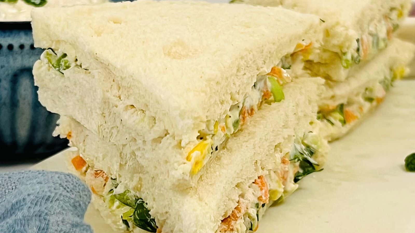 Close-up view of a stack of Yogurt Sandwich with white bread, filled with tuna salad and crisp vegetables.