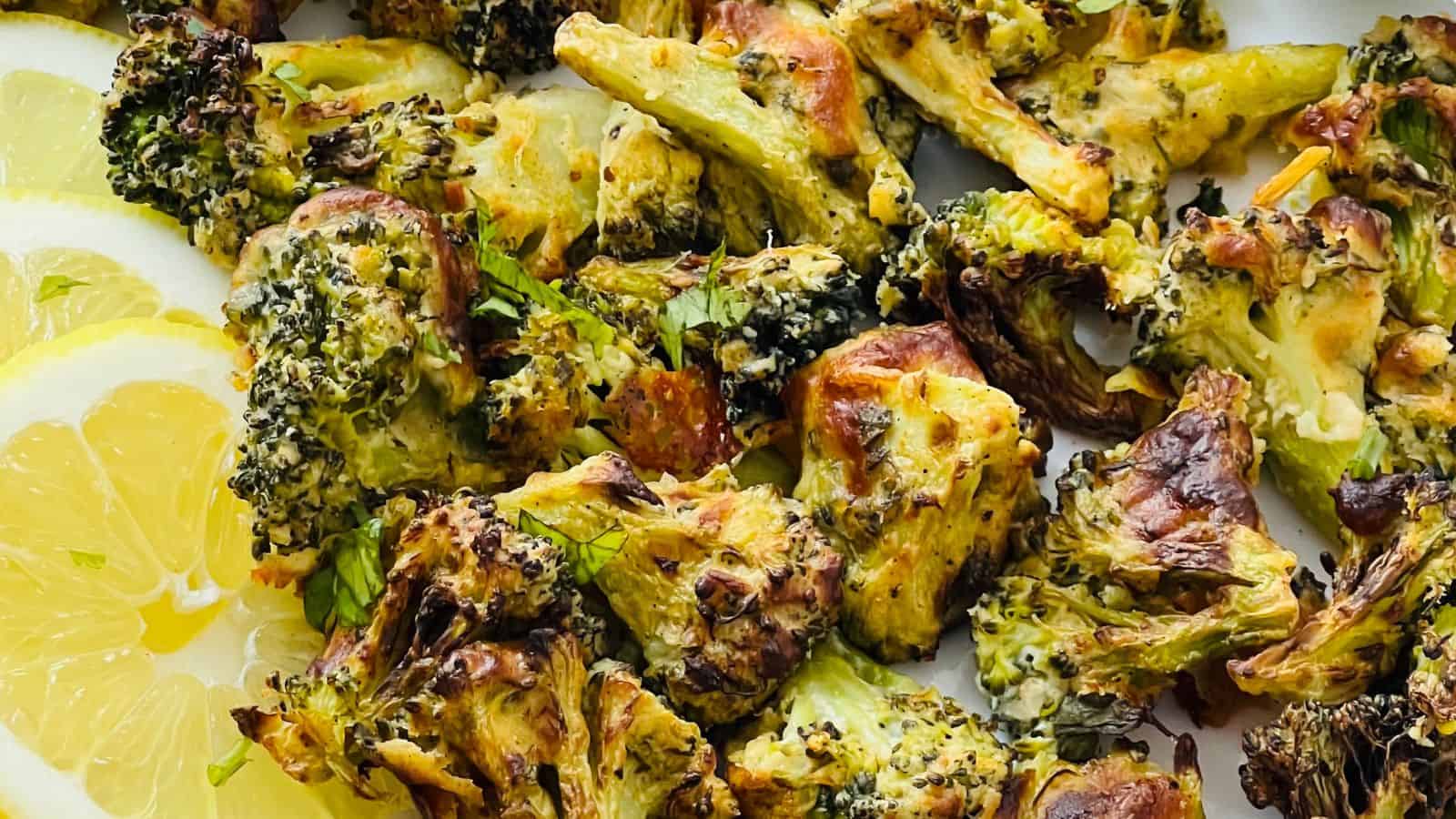 Close-up of roasted broccoli florets seasoned and slightly charred, accompanied by slices of lemon on the side.