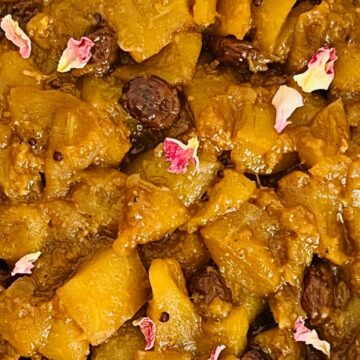 A close-up of a dish featuring cooked yellow squash and raisins, garnished with pink flower petals.