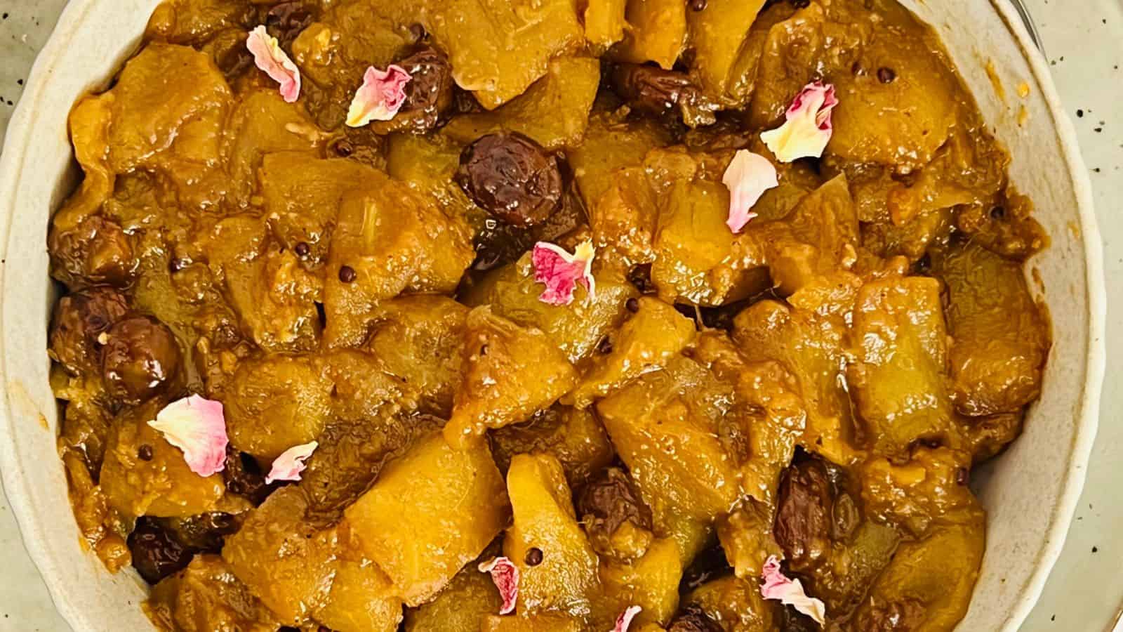 A close-up of a dish featuring cooked yellow squash and raisins, garnished with pink flower petals.