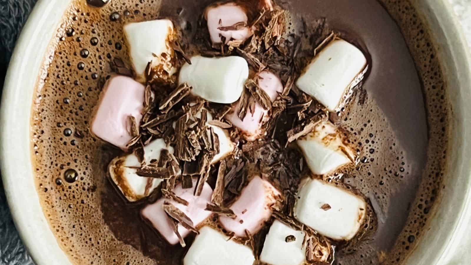 A bowl of hot chocolate topped with pink and white marshmallows and chocolate shavings.