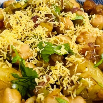 A bowl of chickpea salad garnished with shredded cheese and herbs, featuring diced vegetables such as tomatoes and possibly potatoes, in a blue and white bowl.