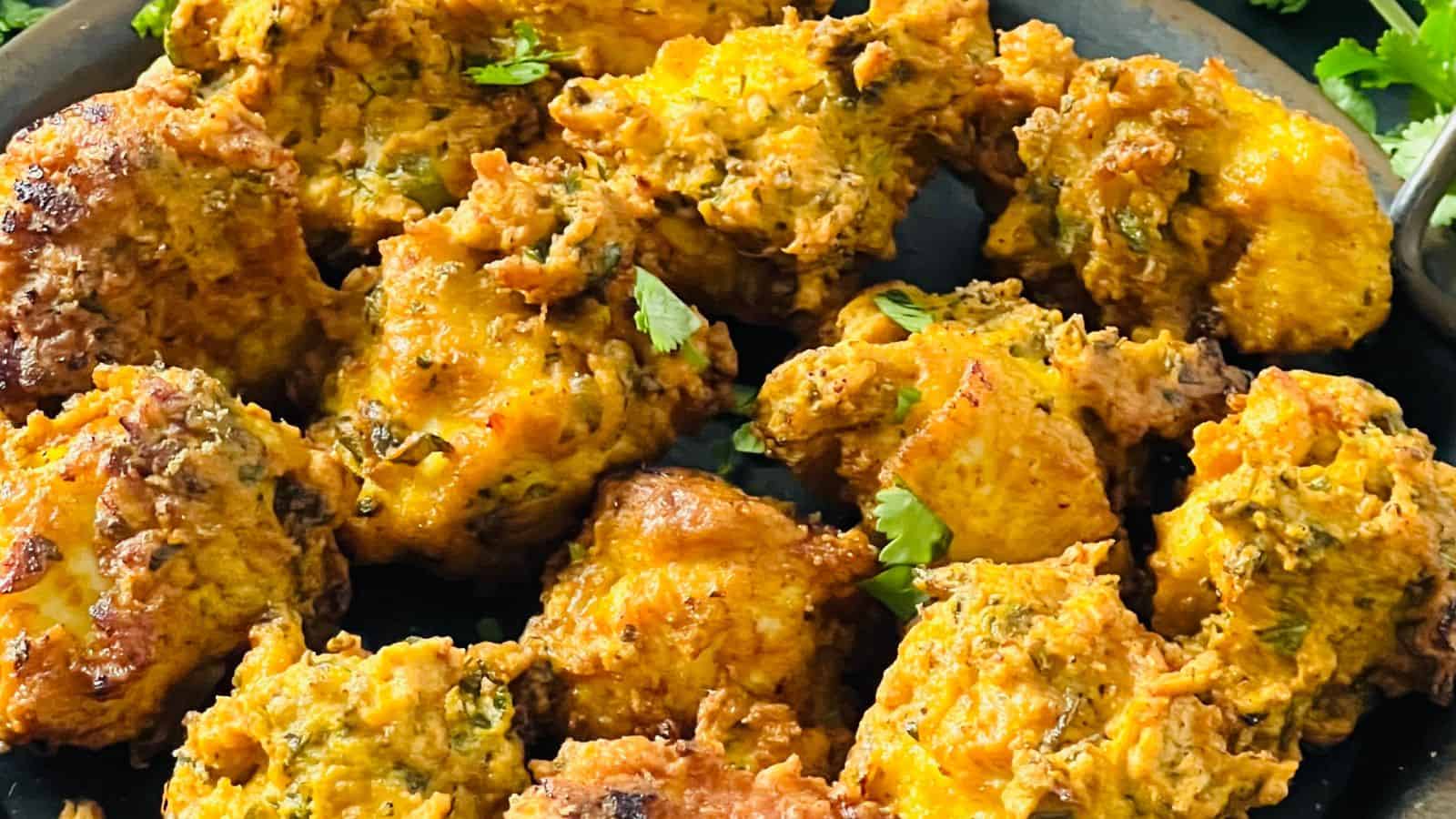 Close-up of a plate filled with golden-brown pakoras, showing their crispy and textured surface, garnished with pieces of cilantro.