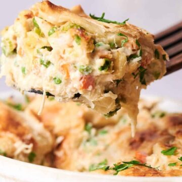 A serving of creamy chicken pot pie casserole with vegetables, lifted on a fork, with a flaky crust and garnished with herbs.