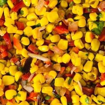 A close-up of a bowl filled with corn salad, featuring yellow corn kernels mixed with diced red bell peppers, onions, and herbs.