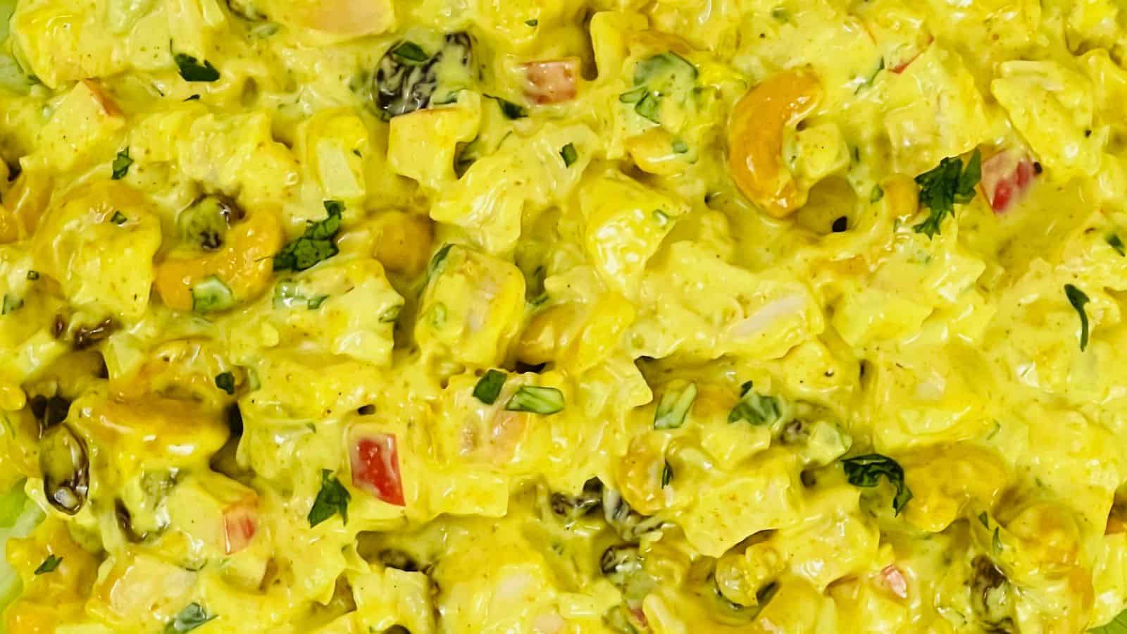 Close-up of a dish featuring a creamy yellow curry with chunks of vegetables, cashews, and raisins, garnished with fresh herbs.