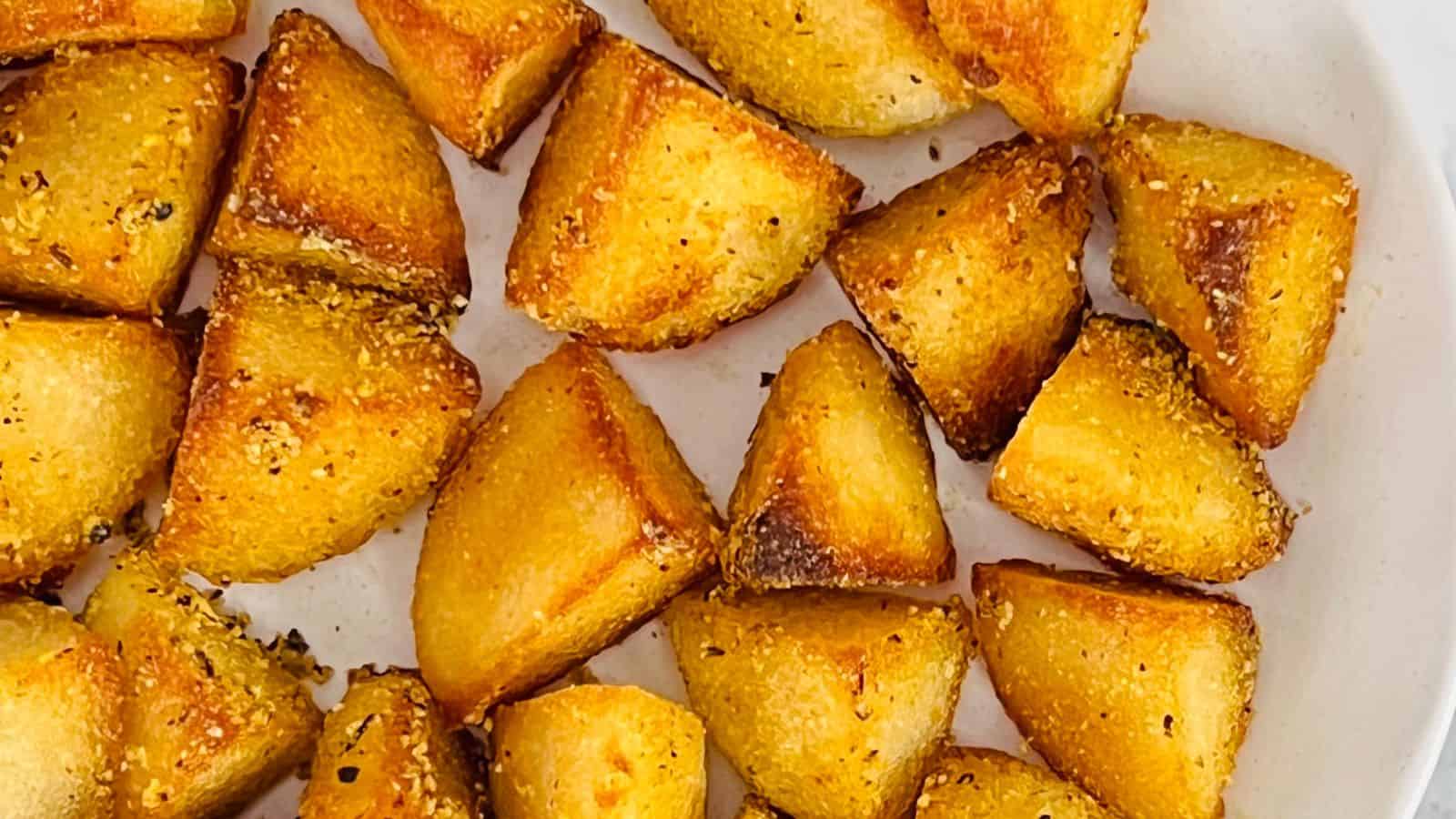 Close-up of roasted potato wedges seasoned with black pepper and spices on a white plate.