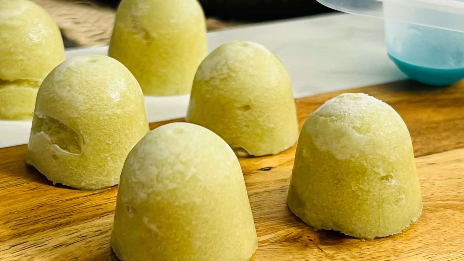 Six yellow, dome-shaped frozen treats placed on a wooden surface.