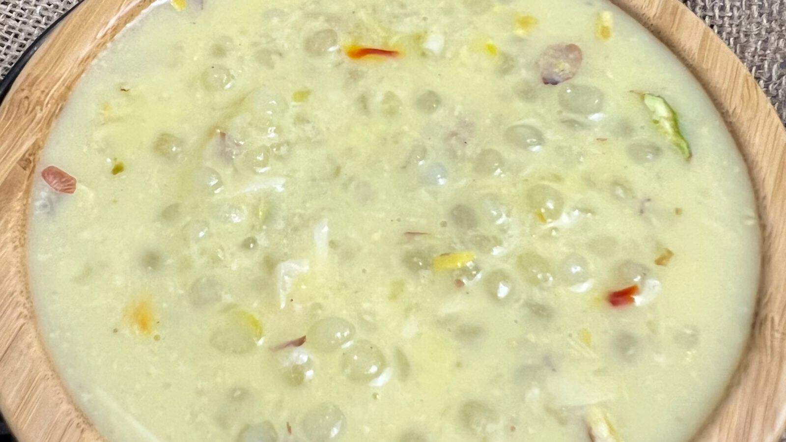 A bowl of creamy soup with visible chunks of vegetables and beans, served in a wooden bowl on a textured placemat.