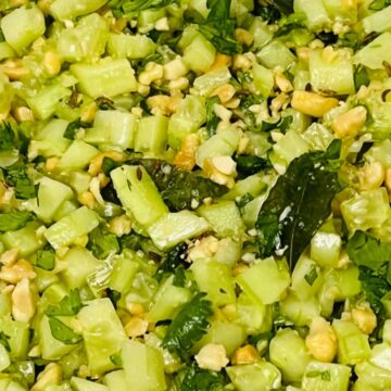 A bowl of chopped cucumber salad mixed with nuts and fresh herbs.