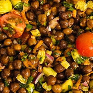 A close-up of a chickpea salad with diced tomatoes, cucumbers, carrots, red onions, and herbs mixed together.