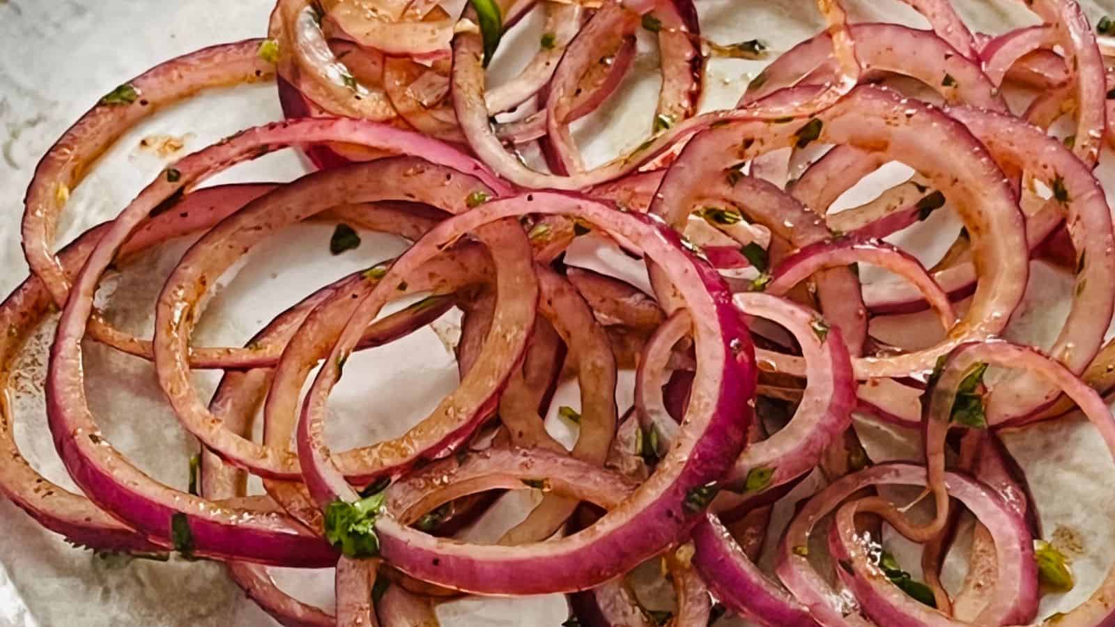 Close-up of thinly sliced red onions, marinated with herbs and spices, placed on a white plate.