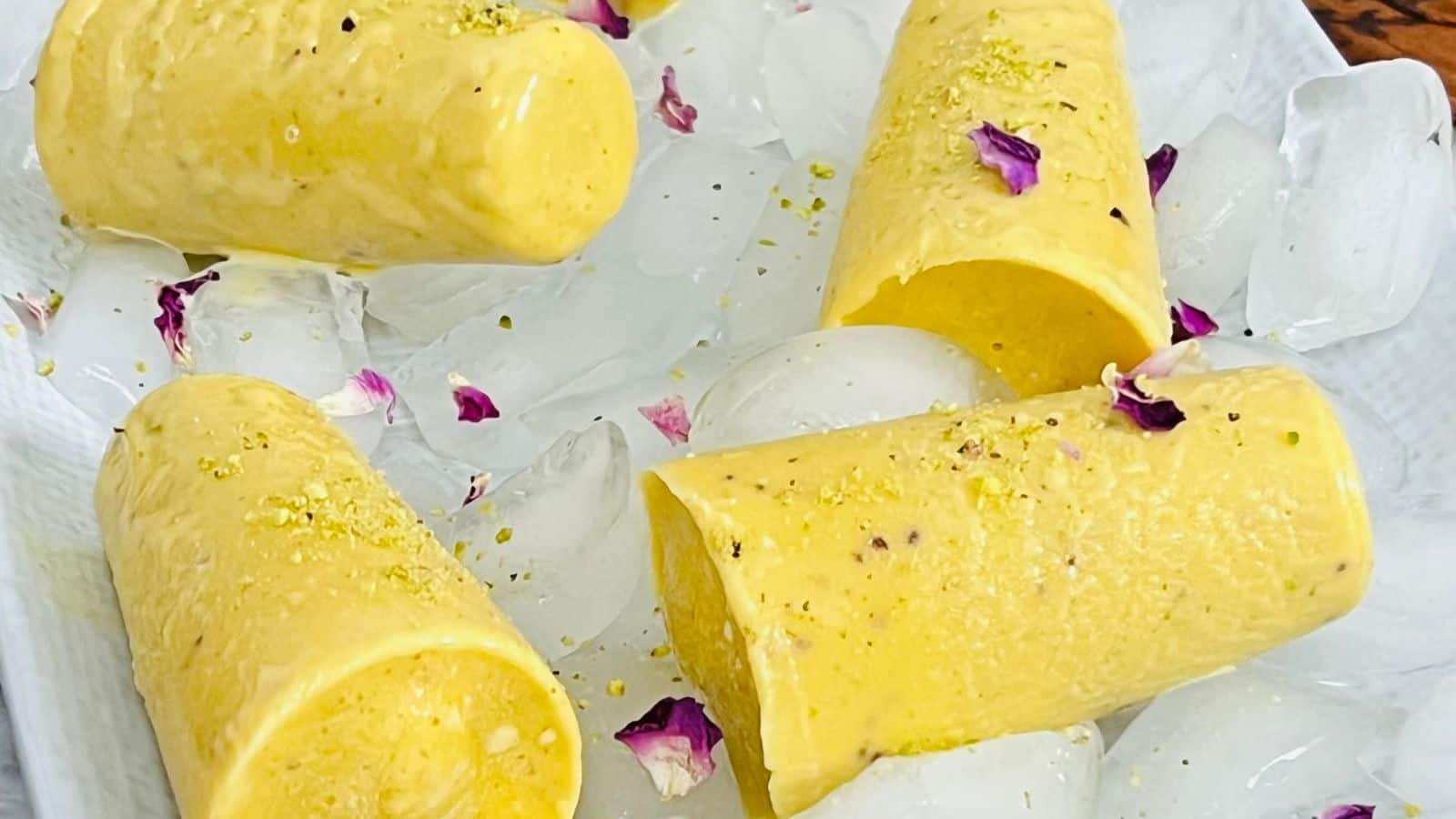 Mango kulfi placed on a black plate on a bed of ice.