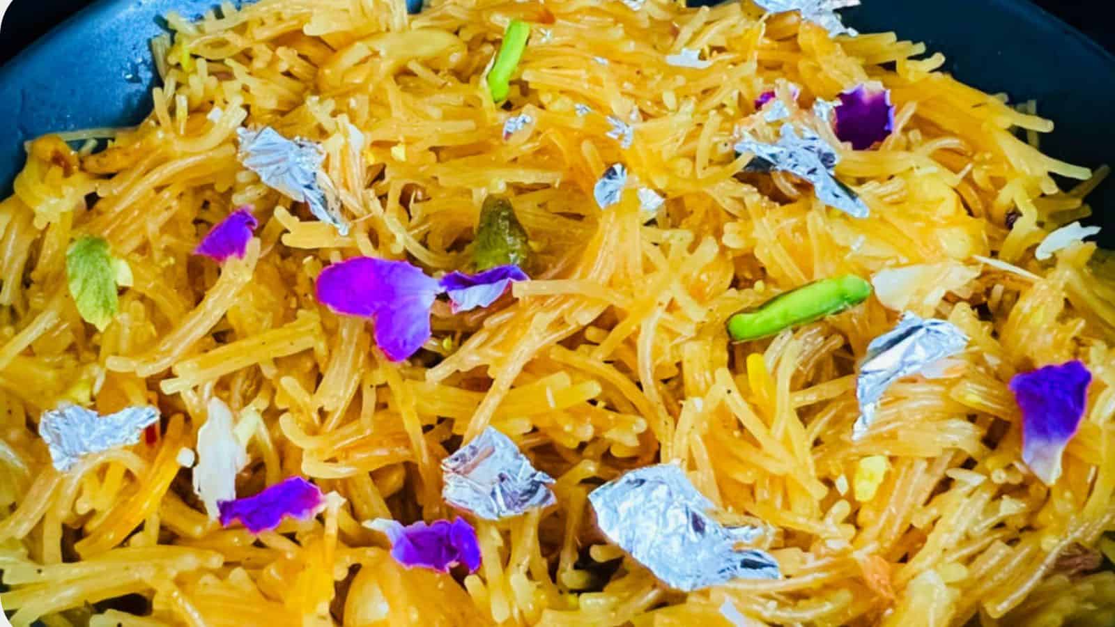 A plate of biryani rice garnished with silver leaf, green chilies, and purple edible flowers.