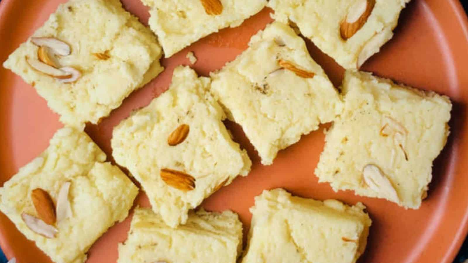 A plate with nine pieces of yellow squares, each garnished with sliced almonds or cashews.