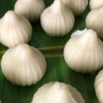 A close-up view of white, steamed modak dumplings arranged on a green banana leaf.