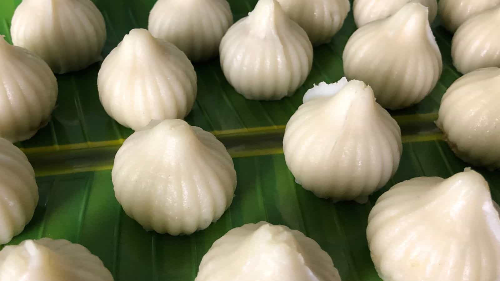 A close-up view of white, steamed modak dumplings arranged on a green banana leaf.