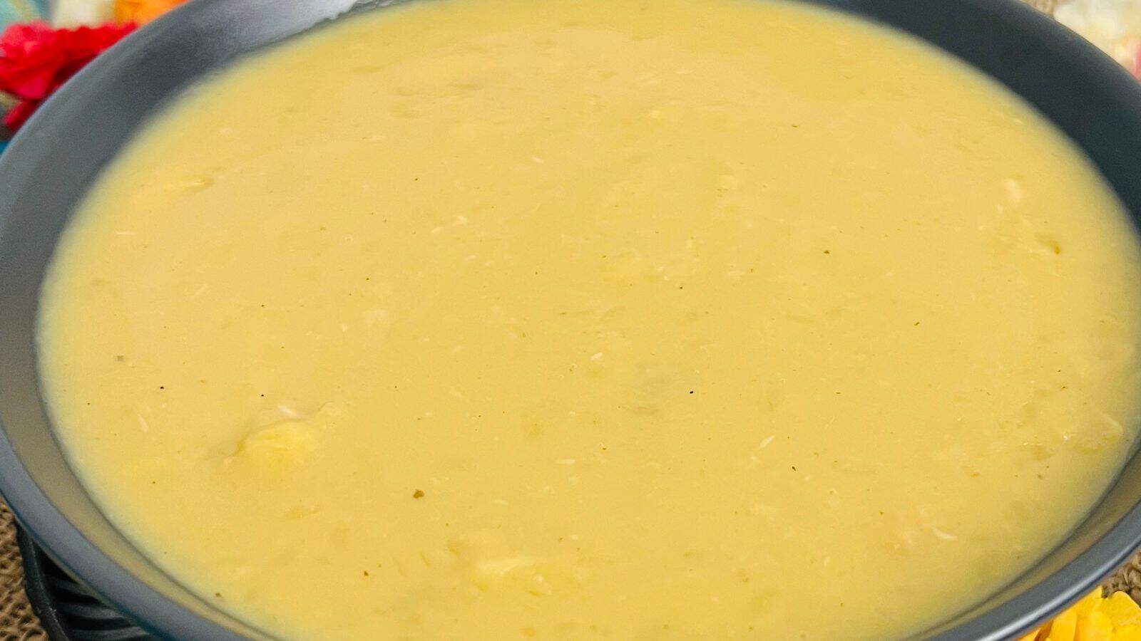 A close-up image of a bowl of creamy yellow soup, presented in a black bowl on a table.