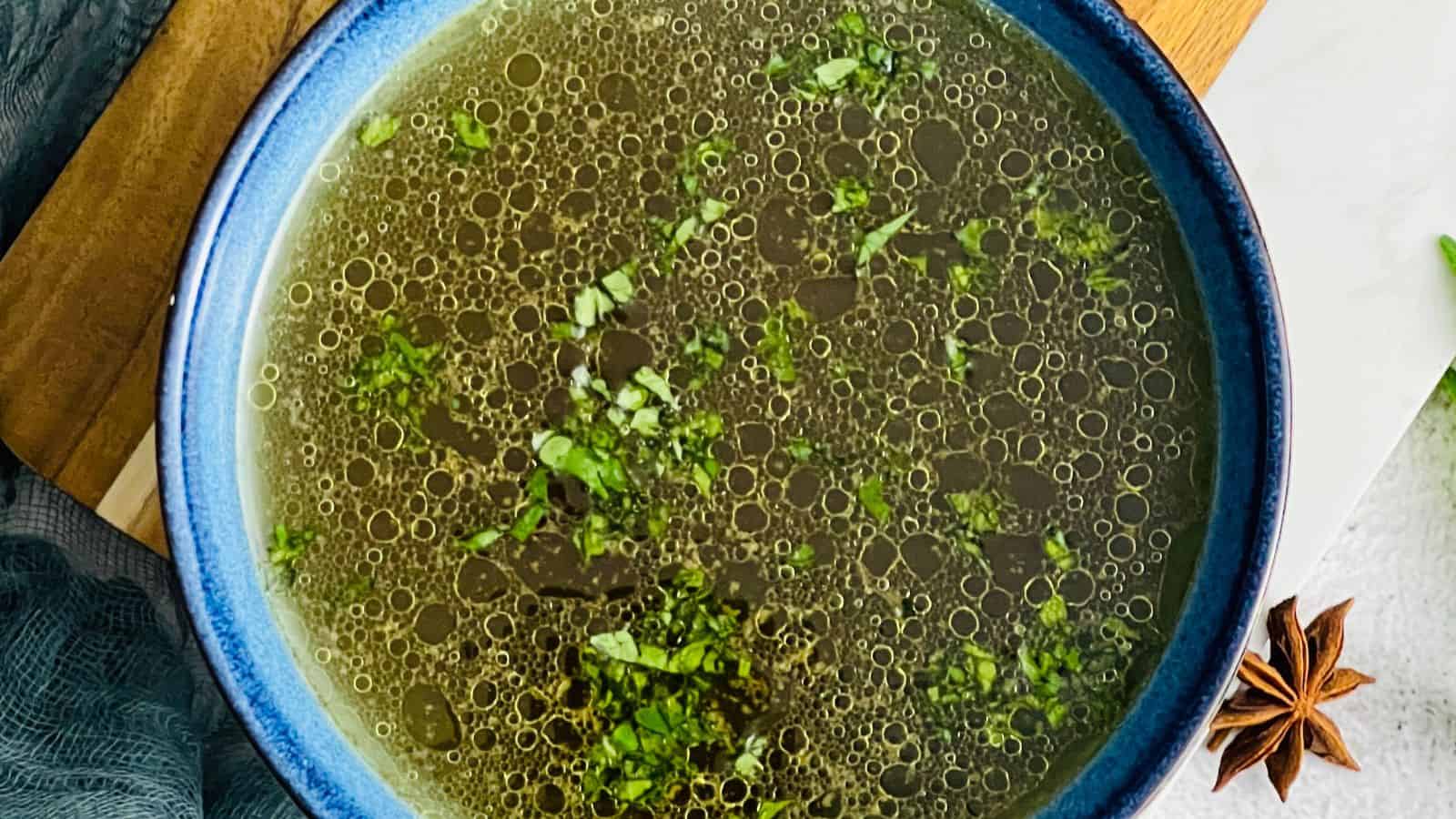 A blue bowl filled with broth, garnished with chopped herbs.