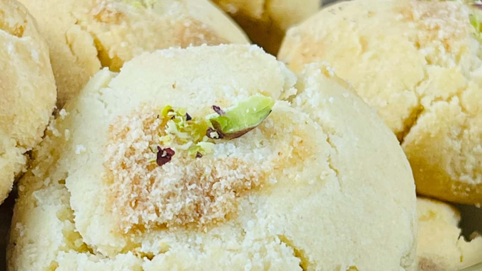 Close-up image of freshly baked cookies sprinkled with chopped pistachios and a hint of powdered sugar.