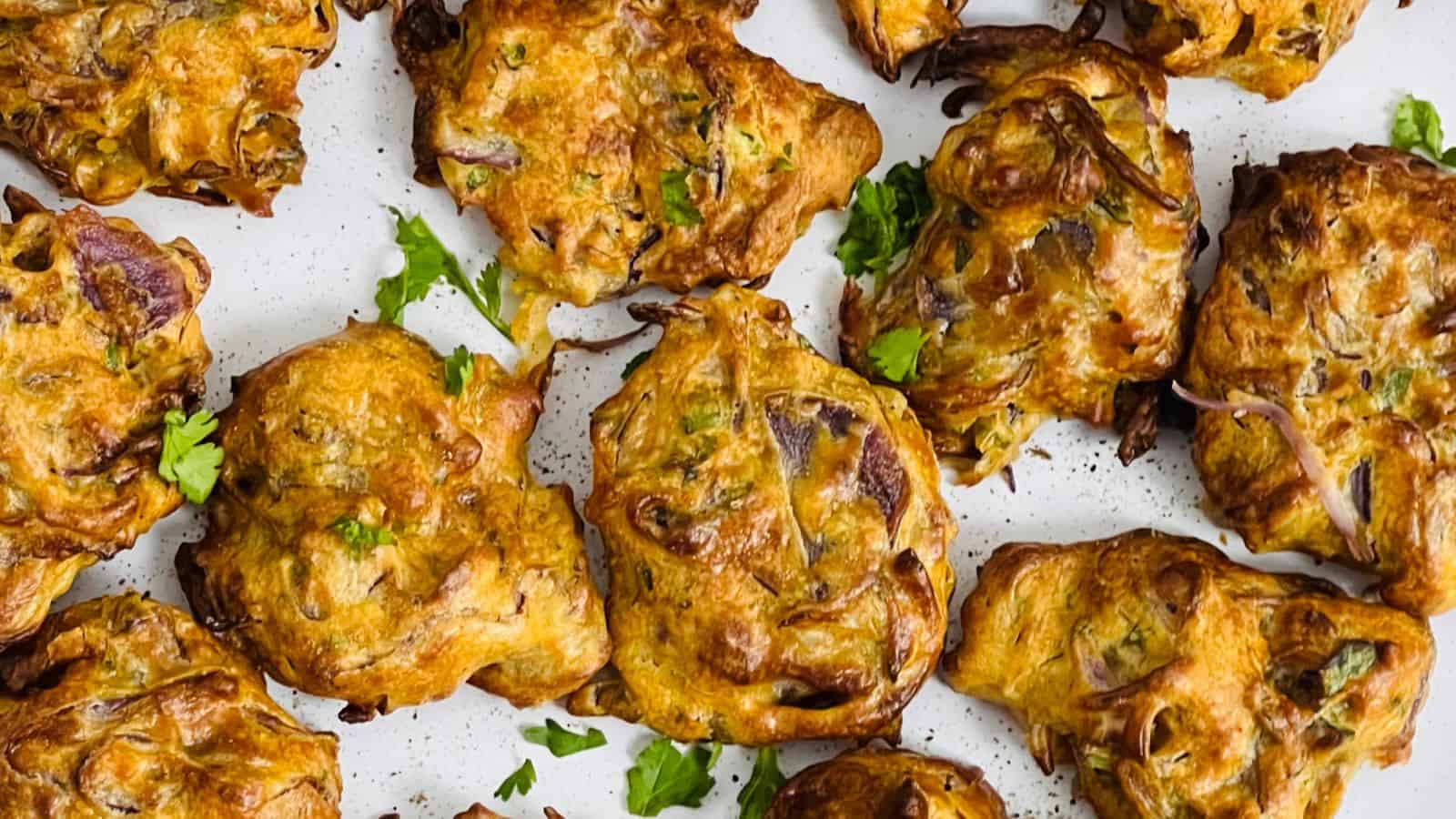 Golden brown onion bhajis garnished with fresh cilantro on a white surface.