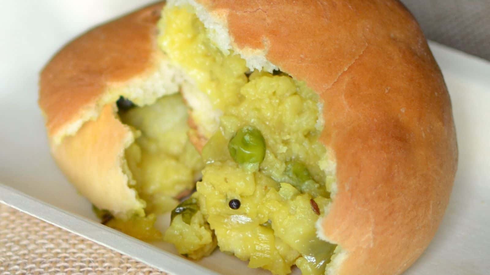 A stuffed bread roll filled with mashed potato, peas, and spices, partially cut open to reveal the filling.