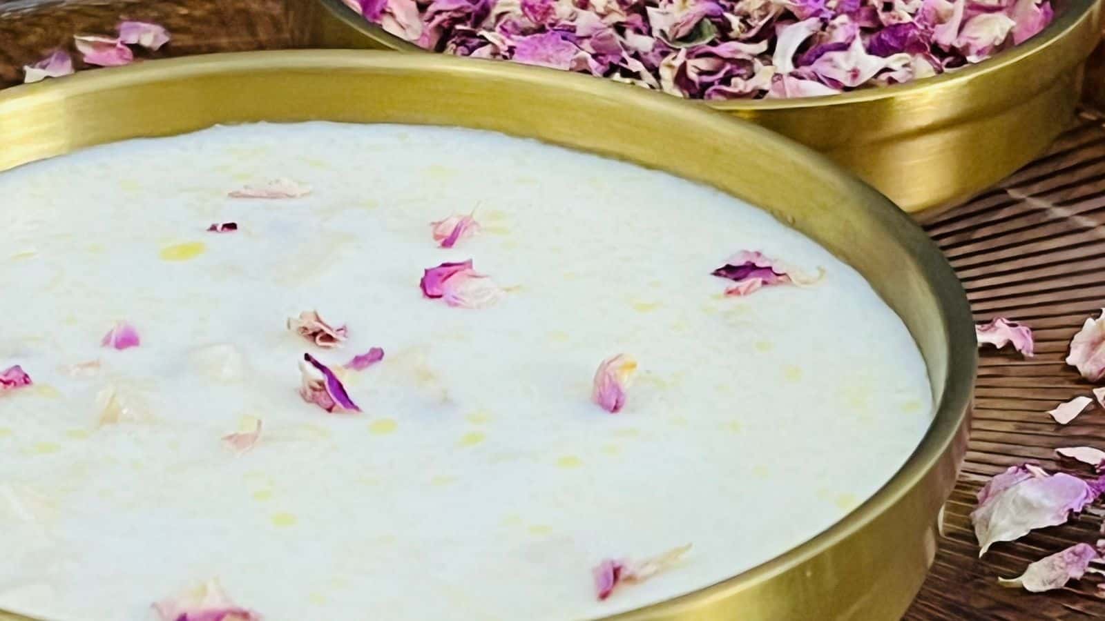 A close-up of a bowl of white dessert garnished with pink rose petals, with a bowl of dried rose petals in the background.