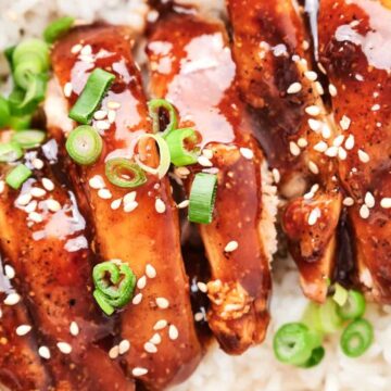 A bowl of rice topped with glazed chicken, garnished with green onions and sesame seeds.