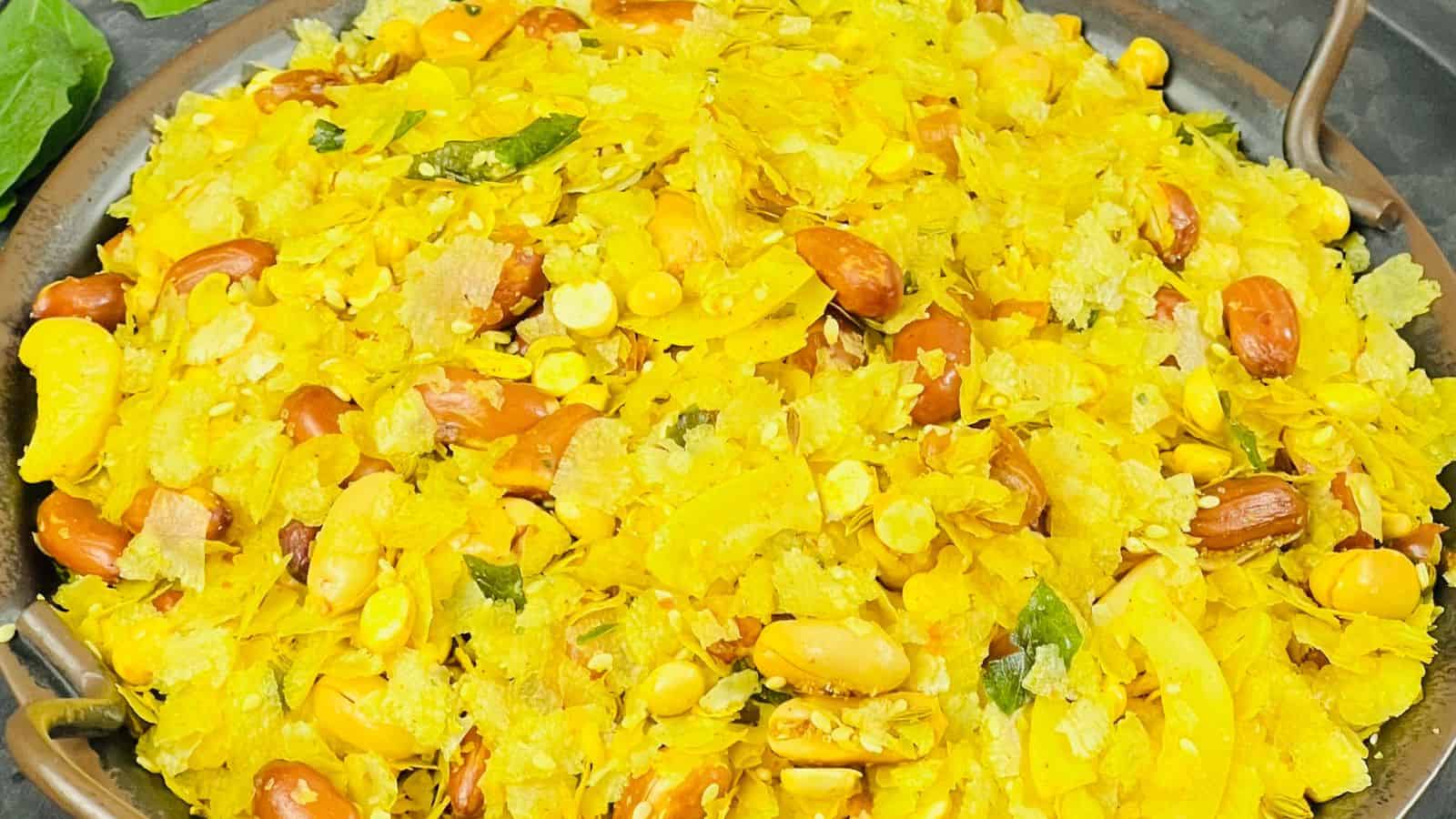 A bowl of bright yellow poha, garnished with peanuts, corn, and green chilies.