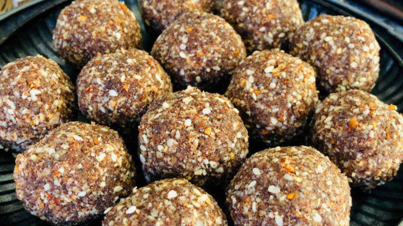 A close-up of a plate containing multiple spherical, textured sweet balls made from sesame seeds and groundnuts.