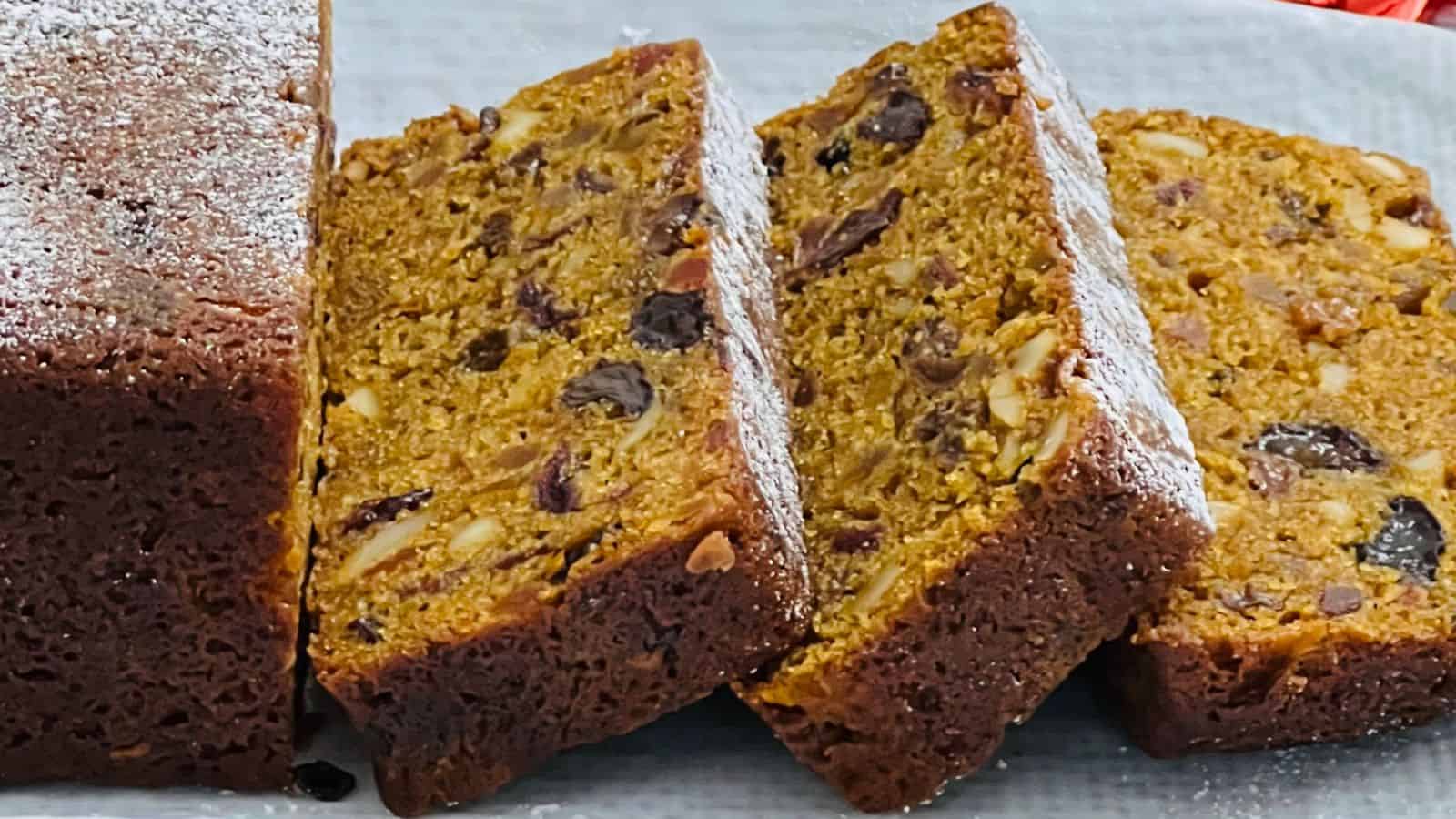 A loaf of fruitcake partially sliced, revealing a dense, moist interior with visible nuts and dried fruits.