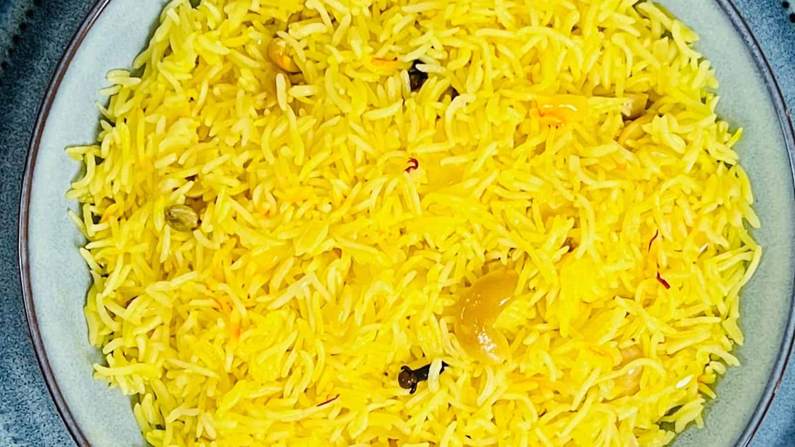 A bowl of cooked yellow rice with visible spices, including cardamom pods and clove.