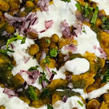 A bowl of chickpeas topped with diced red onions, fresh herbs, dollops of yogurt, and a green herb sauce.