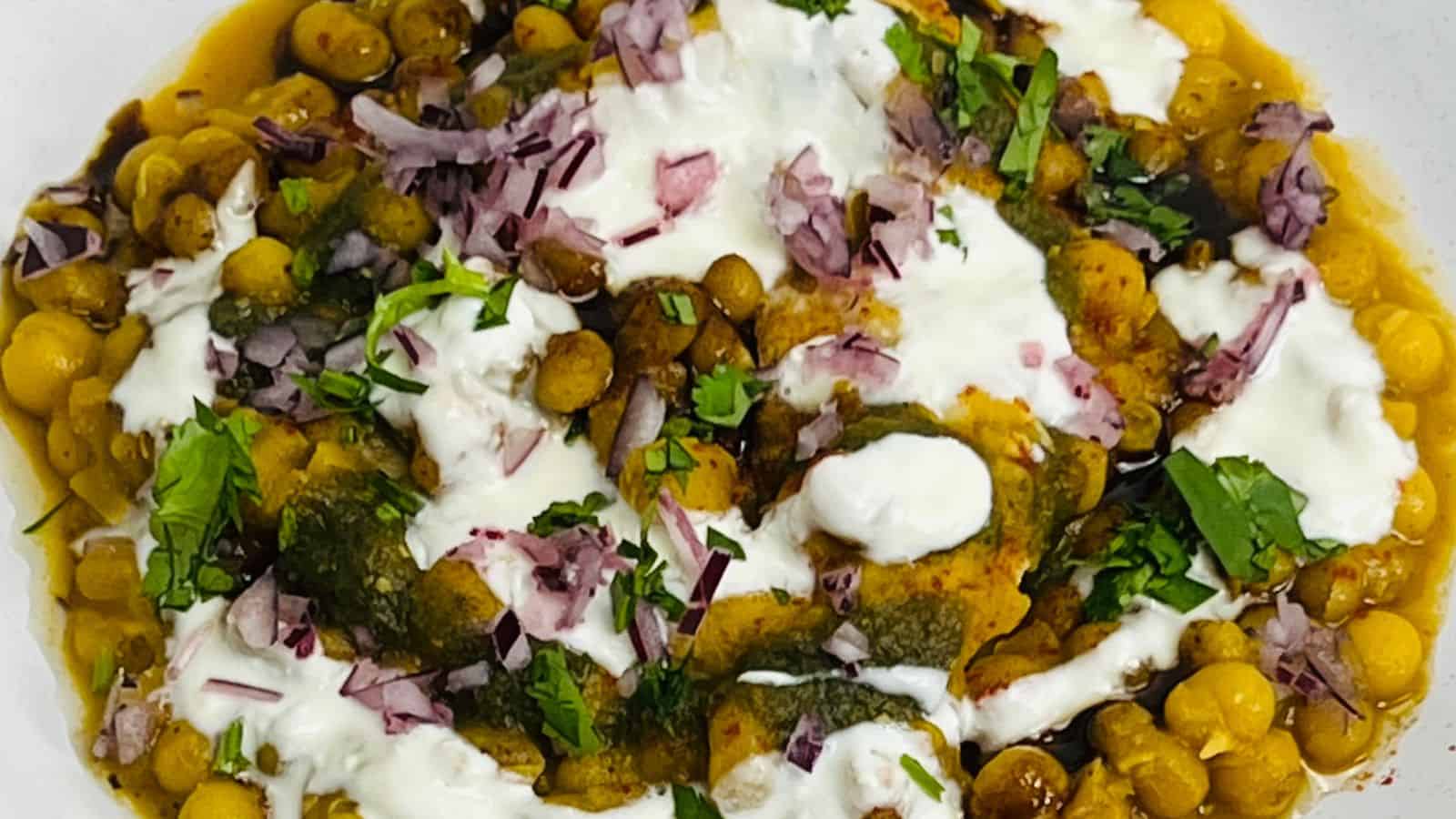 A bowl of chickpeas topped with diced red onions, fresh herbs, dollops of yogurt, and a green herb sauce.