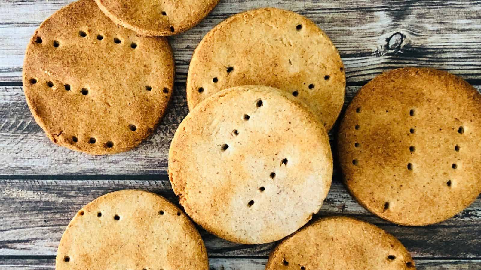 Seven pieces of round, evenly-baked biscuits with small holes arranged on a wooden surface.