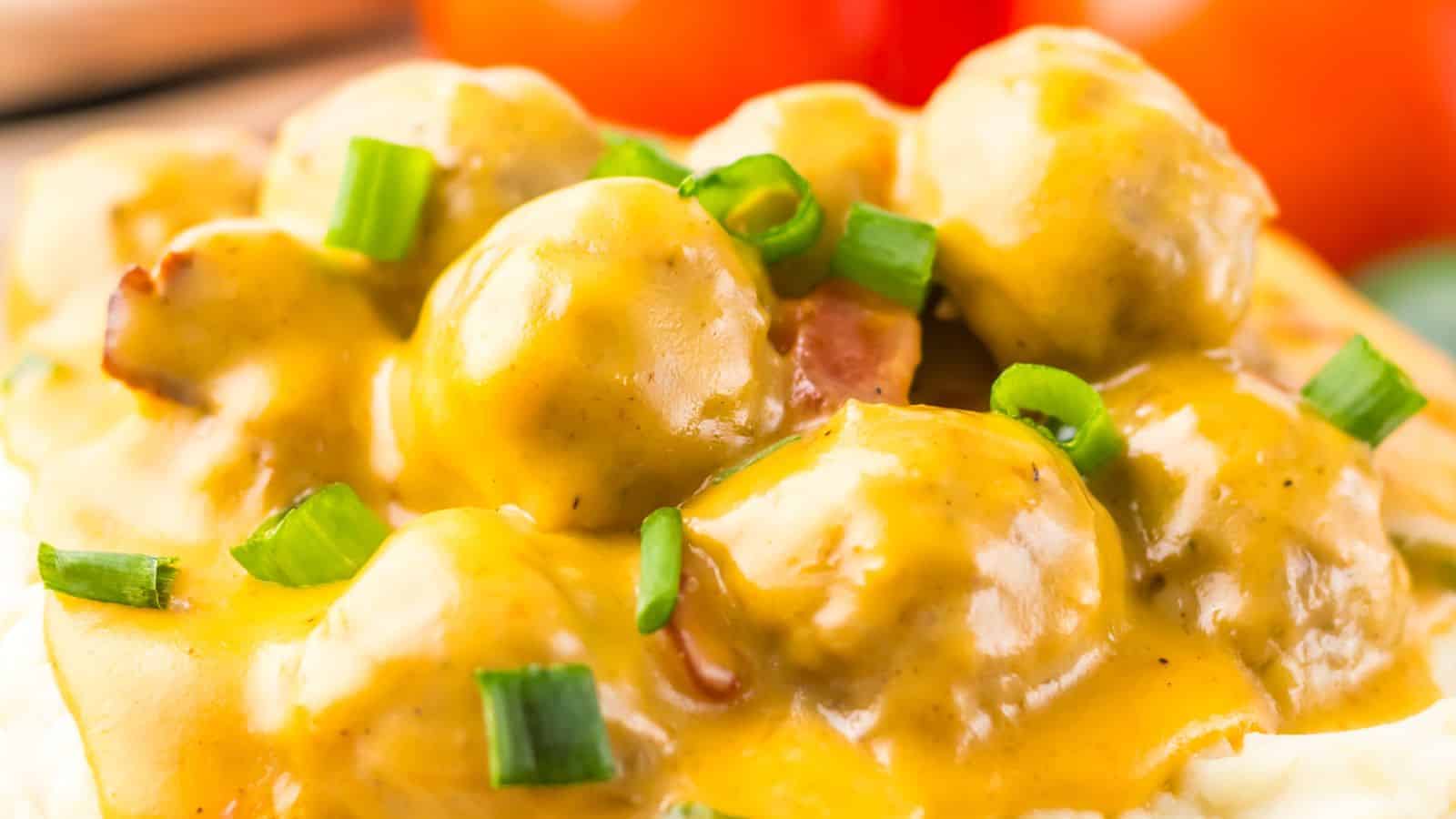 Close-up of meatballs covered in a rich, creamy yellow sauce, garnished with chopped green onions.