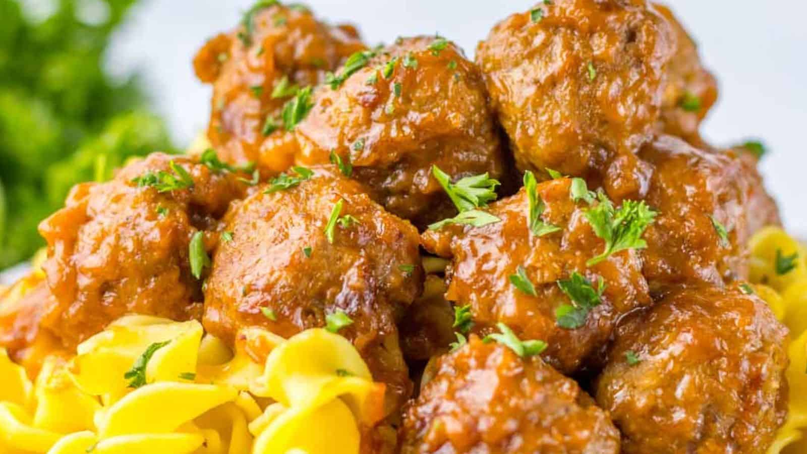 A close-up of saucy Salisbury steak meatballs served on a bed of egg noodles, garnished with chopped fresh herbs.